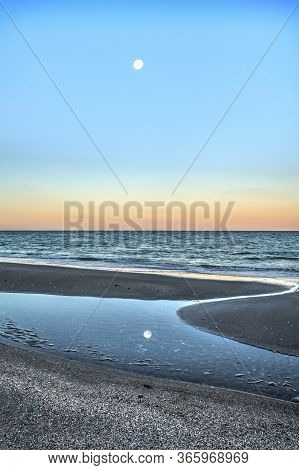 Reflection Of The Full Moonset In A Tidal Pool In Front Of The Ocean On Naples Beach In Naples, Flor