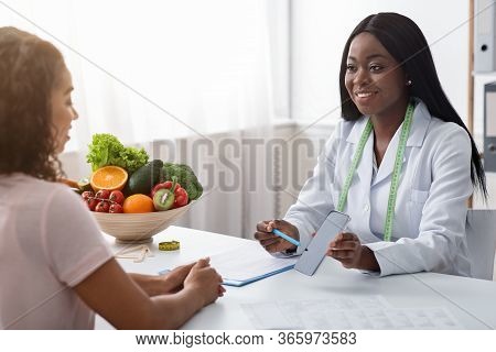 African Woman Dietologist Showing Patient Blank Smartphone Screen, Mobile App For Counting Calories,