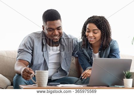 Young African American Couple Planning Budget Together At Home, Writing Notes To Notebook, Creating 