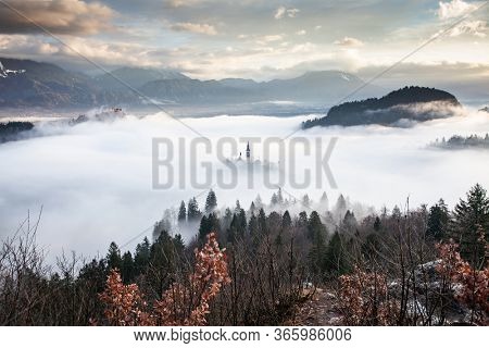 amazing panorama of Lake Bled Blejsko Jezero on a foggy morning with the Pilgrimage Church of the Assumption of Maria on a small island and Bled Castle and Julian Alps in backgroud
