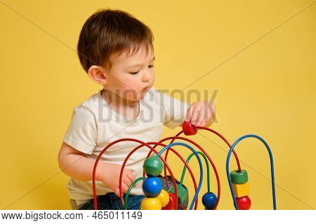 Toddler Baby Is Playing Logic Educational Games On A Studio Yellow Background. Happy Child Play With