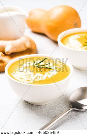 White Bowl With Thick Butternut Squash Bisque Garnished With Heavy Cream And Rosemary On Gray Concre