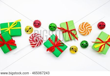 Happy Holidays: Gifts With Lollipops And Red, Green, Golden Bells On A White Background, Copy Space.