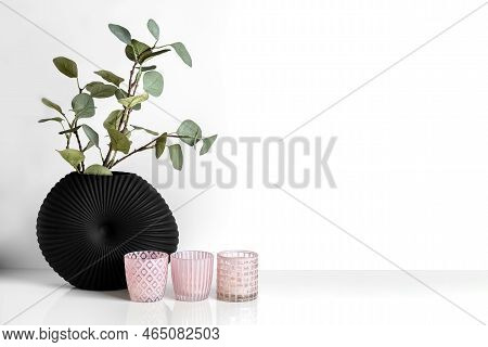 Three Pink Candlesticks And A Eucalyptus Branch In A Black Vase On A White Background. Photo