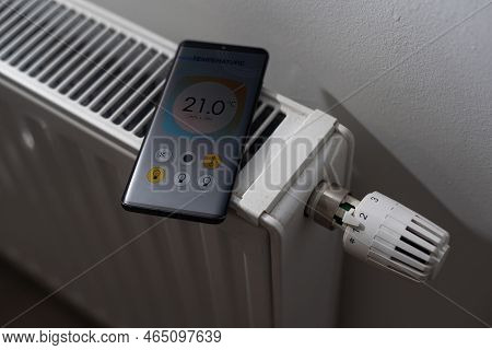 Smartphone With Launched Application For Air Temperature Adjustment Opposite The Radiator. Health Mi