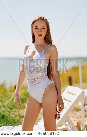 A Long-haired, Slender, Beautiful Woman In A Swimsuit By A Chaise Longue By Sea.