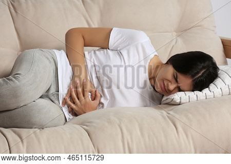 Young Woman Suffering From Menstrual Pain On Sofa Indoors
