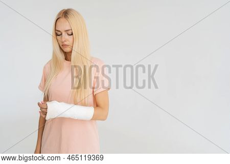 Studio Portrait Of Unhappy Injured Blonde Young Woman With Broken Arm Wrapped In Plaster Bandage Loo