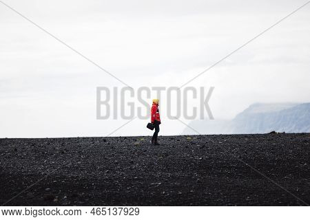 Traveler In A Red Jacket Standing On A Black Sand Beach In Iceland