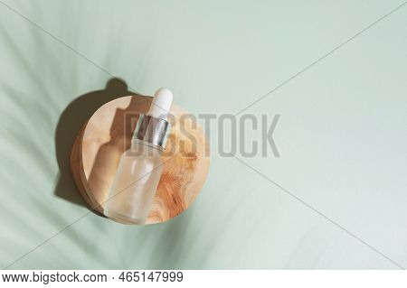 Cosmetic Bottle With Pipette On Wooden Slice Top View, Flat Lay On Colored Background With Palm Shad