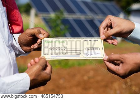 Focus On Hand, Close Up Shot Of Farmer Receiving Check From Banker In Front Of Solar Panel - Concept
