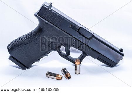 A Black 9mm Pistol With Three 9mm Hollow Point Bullets On A White Background