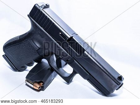 A Black 9mm Pistol With A Loaded Magazine Underneath It On A White Background