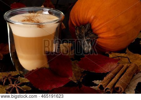 Heat-resistant Glass Cup With Cappuccino Or Latte And Ripe Pumpkin Stand On A Stand With Autumn Leav