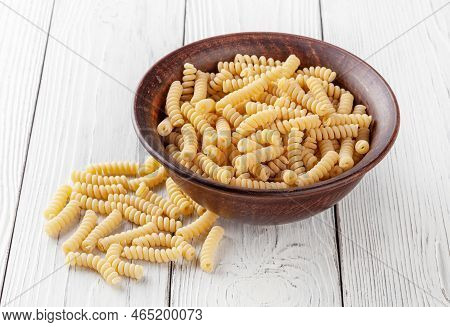 Uncooked Fusilli Pasta In Ceramic Bowl On White Wooden Background