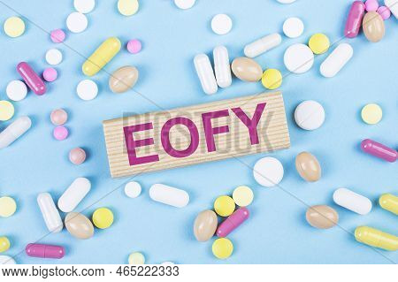 On A Blue Background, Multi-colored Pills And A Wooden Block With The Text Eofy. View From Above. Me