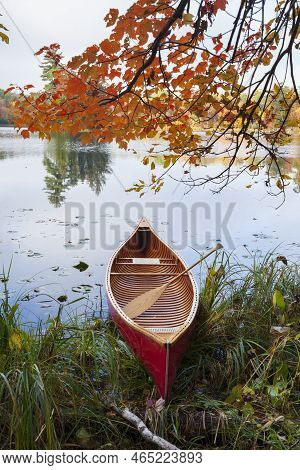 Red Wooden Canoe On Calm Lake With Maple Branches Above During Autumn