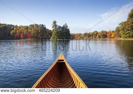 Wooden Canoe Moves On A Blue Lake With Trees In Autumn Color And A Small Island In Northern Minnesot