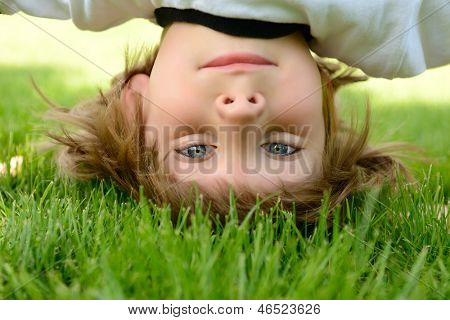 Glückliche kleine Junge stehend Kopf auf grünem Gras im Frühlingspark.