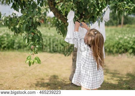 The Child Helps With Household Chores Around The House. A Girl Hangs Snow-white Laundry After Washin