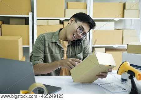 Young Male Small Business Enrtrepreneur, Online Store Owner Working On Laptop With Boxes On Desk At 