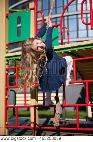 Adorable Blond Female Child Playing On Climbing Frames, Smiling In Sunny Day. Cheerful Girl Climbing