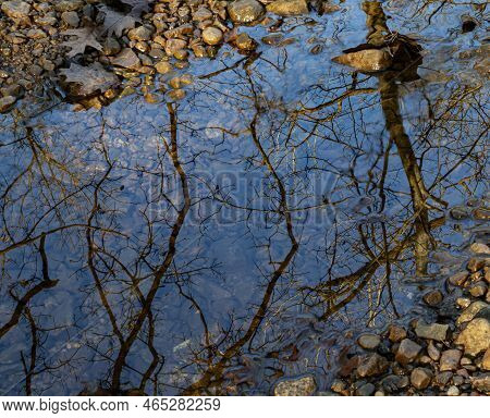 Reflections Of Trees And A Blue Sky Appear Between Rocks And Stones In Sawmill Creek, Waterfall Glen