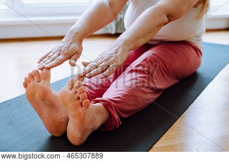 Unrecognizable Curvaceous Adult Woman, With Blond Long Hair, Doing Stretching Exercise On Sports Mat