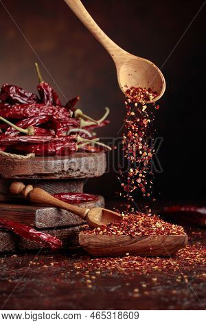 Chilli Flakes Are Poured Into A Wooden Dish. Chilli Flakes And Dried Chili Peppers On A Brown Backgr