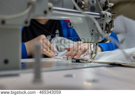 Close-up Of The Sewing Process. Womens Hands Stitching Beige Fabric On A Professional Production Mac