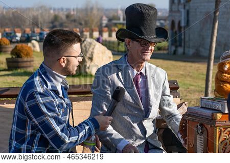 Bendery, Moldova - November 12, 2022: Organ Grinder In A Hat And Round Glasses Gives An Interview On