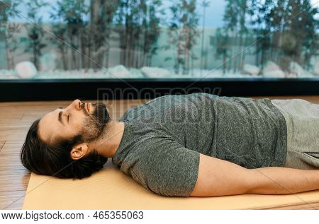Savasana Or Corpse Dead Pose. Handsome Man Relaxes In Motionless Corpse Pose With Closed Eyes Lying 