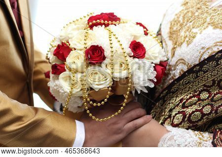 Man And Woman Holding A Bouquet Of Rose Red And White Flowers While Holding Hands In Wedding.