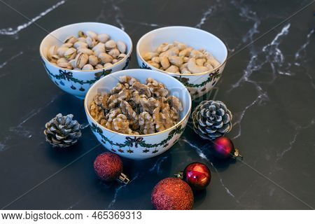 Three Bowls Of Christmas Godies On The Table. Pistachio, Walnuts And Cashwe Nuts In Christmas Bowls.