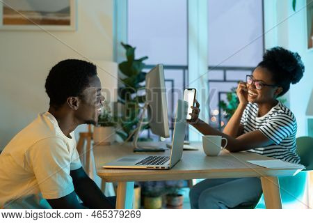 Happy Laughing African American Woman Showing Mobile Phone Screen Man To Friend Sits At Table With L