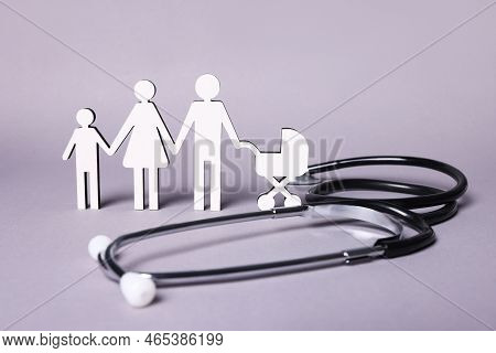 Figures Of Family Stainding Near Stethoscope On Lilac Background. Insurance Concept