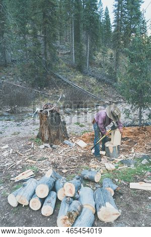 Ranchhand Boy Cuts And Splits Logs While At A Campsite In The Forest, Using An Axe