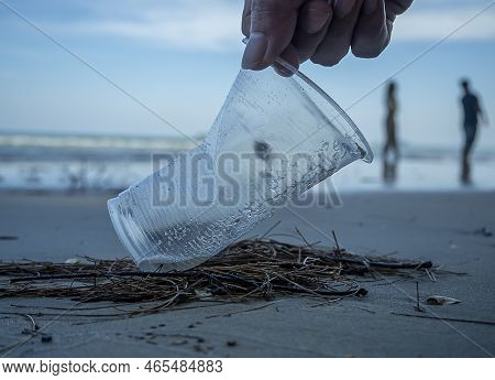 Hand Of Man Picking Up Plastic Cup Cleaning On The Beach.  Volunteer Clean The Trash On The Beach Ma