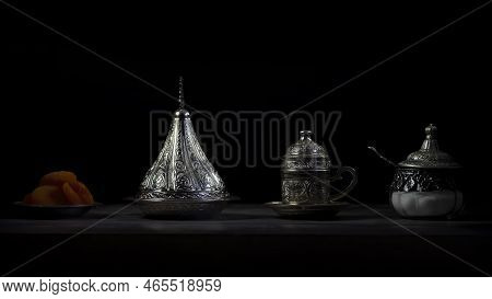 Silver Coffee Cup And Sugar Jars With Dates And Dried Apricots, Dark Background.
