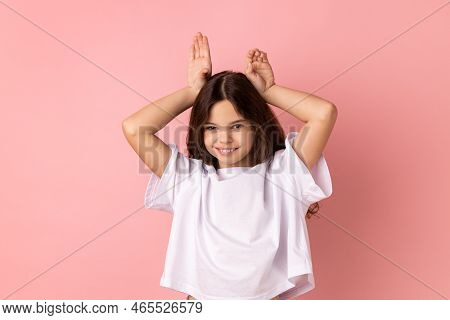 Portrait Of Positive Little Girl Wearing White T-shirt Making Funny Bunny Ears With Hands On Head, C