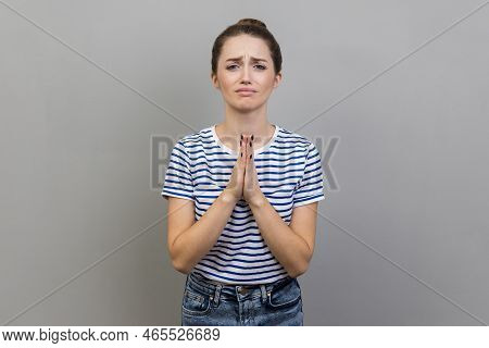 Please, I Need. Portrait Of Woman Wearing Striped T-shirt Holding Hands In Prayer And Asking For Hel
