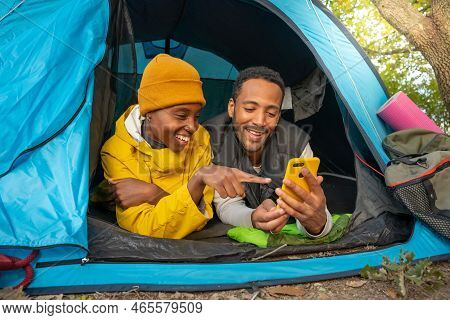 Happy Black Couple Using Cellphone And Sitting In Tent During Camping Having Fun Together