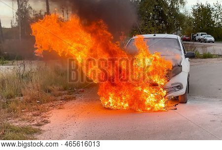 Accident. A White Car In An Industrial Area Is On Fire. The Engine Compartment Is On Fire. Defocused