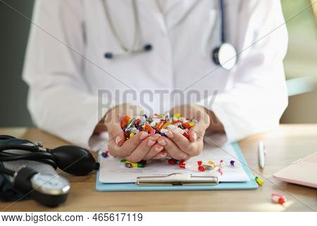 Female Doctor Sitting At Desk And Holding Many Pills And Drung In Hands. Woman Pharmacist Reviewing 