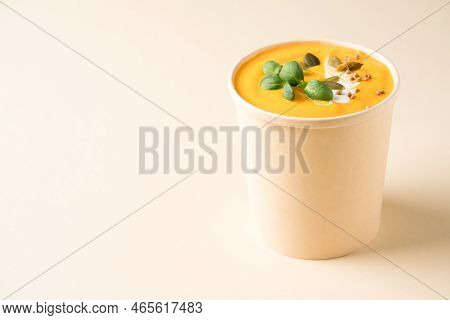 Creamy Pumpkin Fall Soup In Craft Paper Food Container Against Light Background With Copy Space. But