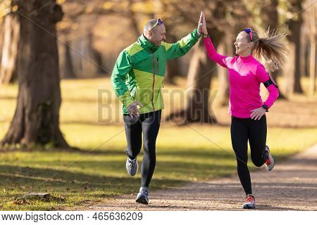 Two Runners Mature Man And Young Woman Support Each Other And Give High-five While A Run.