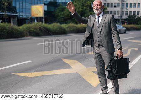 Senior Businessman With Laptop Bag Gesturing While Hailing For Taxi Cab In The City Streets.