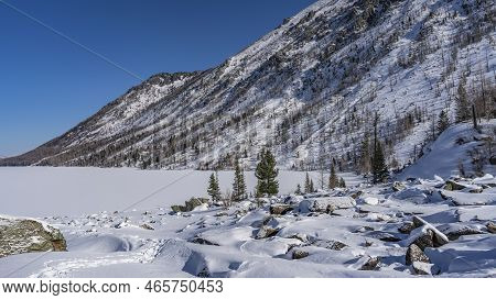 The Surface Of The Frozen Lake Is Covered With Pure Untouched Snow. Picturesque Boulders Are Scatter