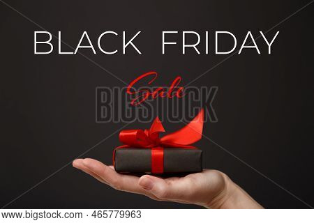 Black Friday Sale. Woman's Hand Holding Black Gift Box With Red Bow Over Black Background. Black Fri