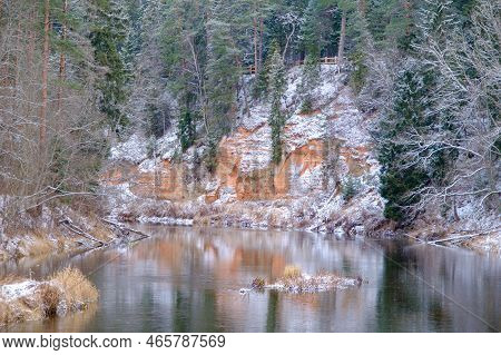 View Of Red Sandstone Cliffs. Salaca River. Skanaiskalns Nature Park. November Is The First Snow In 